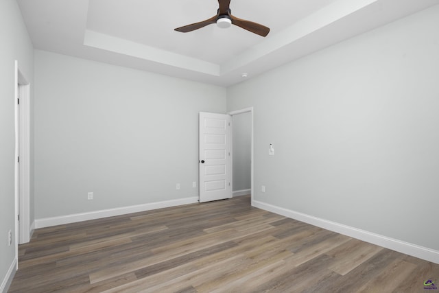 unfurnished room with baseboards, a tray ceiling, a ceiling fan, and wood finished floors