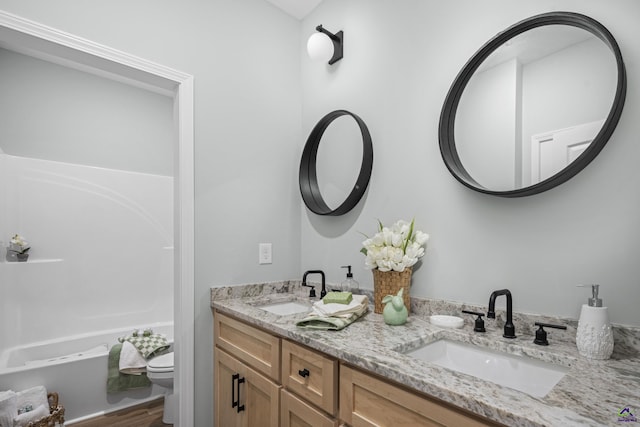 bathroom with toilet, wood finished floors, double vanity, and a sink