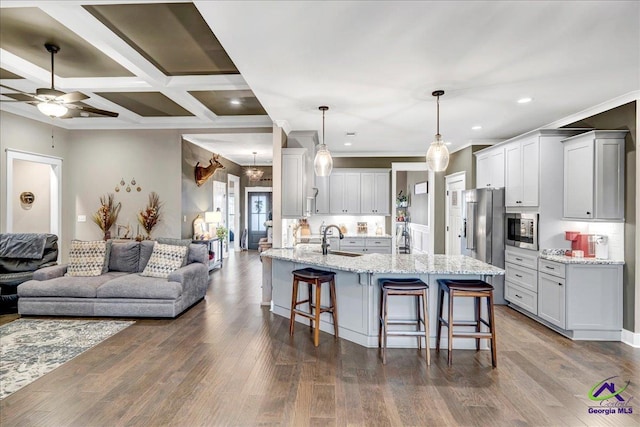 kitchen with a breakfast bar area, a sink, open floor plan, crown molding, and appliances with stainless steel finishes