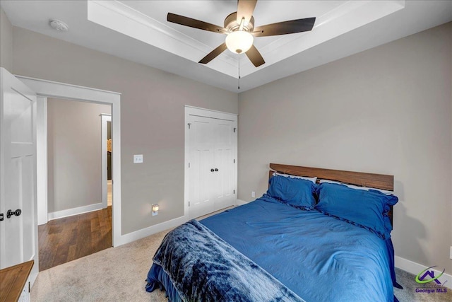 bedroom featuring a tray ceiling, carpet, baseboards, and ceiling fan