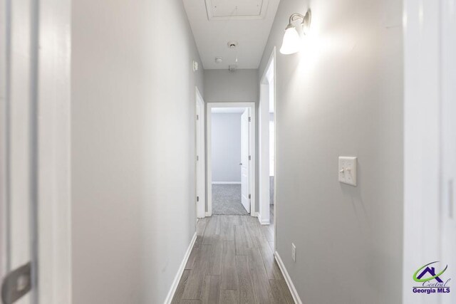 hallway featuring attic access, wood finished floors, and baseboards