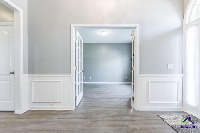 hall with wood finished floors, a wainscoted wall, and plenty of natural light