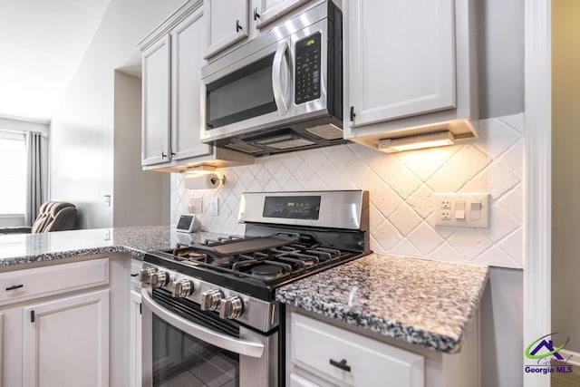 kitchen with light stone counters, stainless steel appliances, backsplash, a peninsula, and white cabinetry