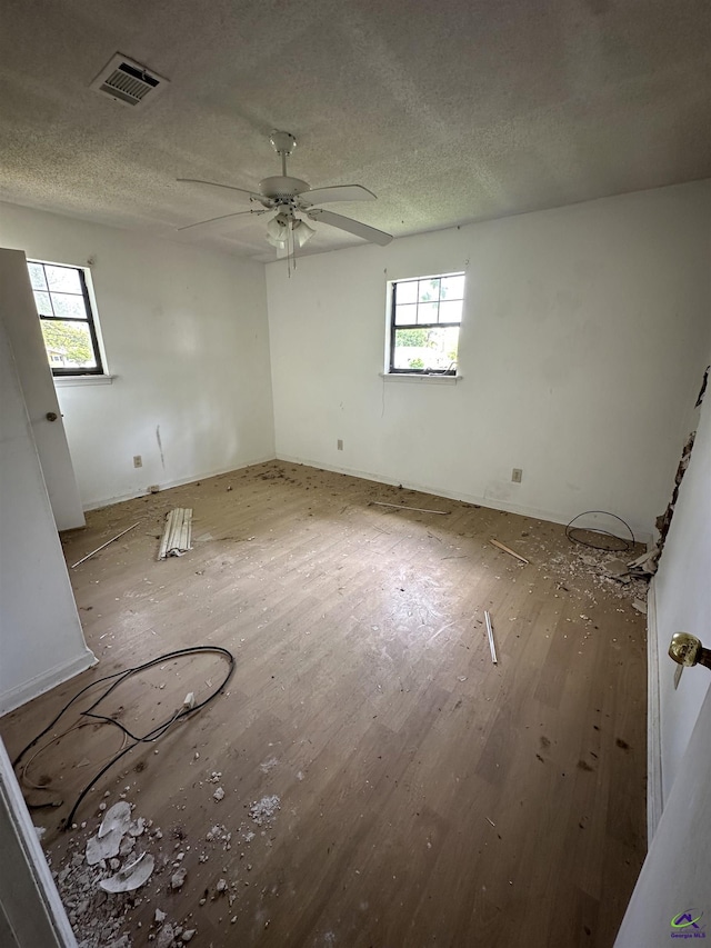 unfurnished room with wood finished floors, visible vents, ceiling fan, and a healthy amount of sunlight