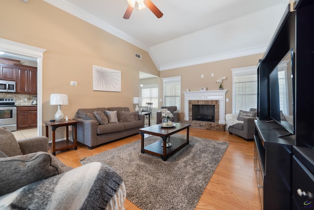 living room with vaulted ceiling, visible vents, a ceiling fan, crown molding, and a fireplace