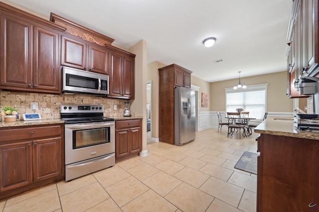 kitchen featuring wainscoting, backsplash, light stone counters, decorative light fixtures, and appliances with stainless steel finishes