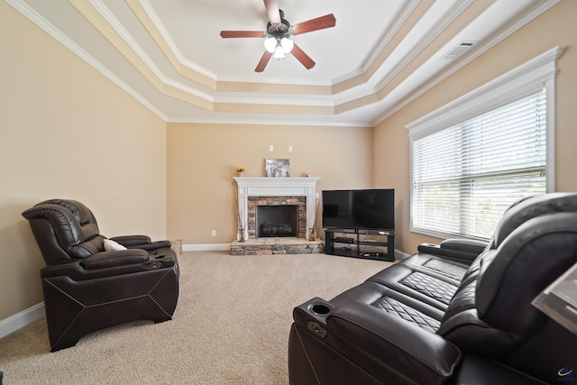 living room featuring a ceiling fan, a stone fireplace, carpet floors, a raised ceiling, and ornamental molding
