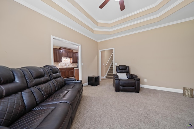 living room with light carpet, baseboards, ceiling fan, crown molding, and a raised ceiling