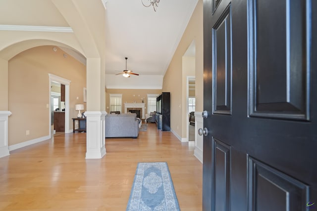 foyer entrance with ornamental molding, a ceiling fan, light wood-style floors, and a fireplace