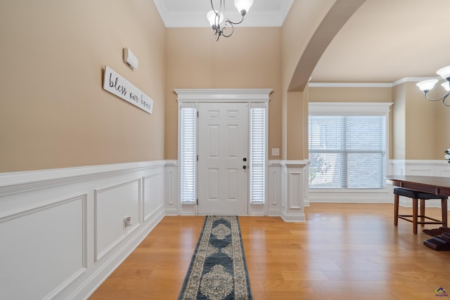 entryway with light wood-style flooring, a wainscoted wall, arched walkways, a notable chandelier, and a decorative wall