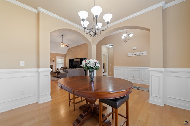 dining space featuring ornamental molding, a wainscoted wall, ceiling fan with notable chandelier, and light wood-style flooring