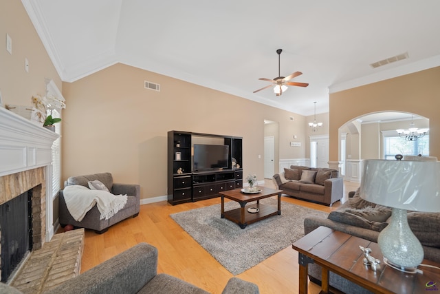 living area with visible vents, arched walkways, crown molding, a fireplace, and ceiling fan with notable chandelier