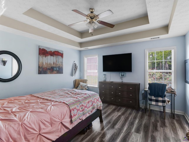 bedroom featuring wood finished floors, visible vents, a ceiling fan, and a tray ceiling
