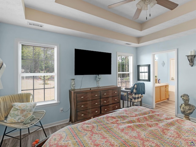 bedroom with a raised ceiling, visible vents, light wood-style flooring, and baseboards