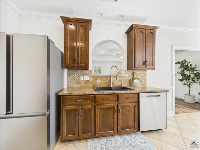 kitchen featuring a sink, light tile patterned floors, tasteful backsplash, crown molding, and appliances with stainless steel finishes