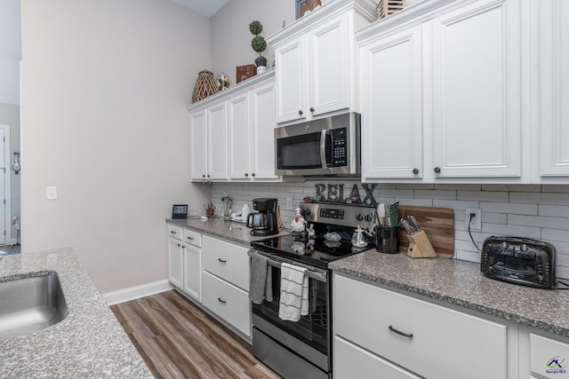 kitchen with dark wood-style flooring, appliances with stainless steel finishes, decorative backsplash, and white cabinetry