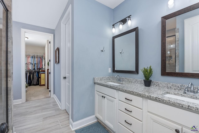 full bath featuring double vanity, a spacious closet, baseboards, and a sink