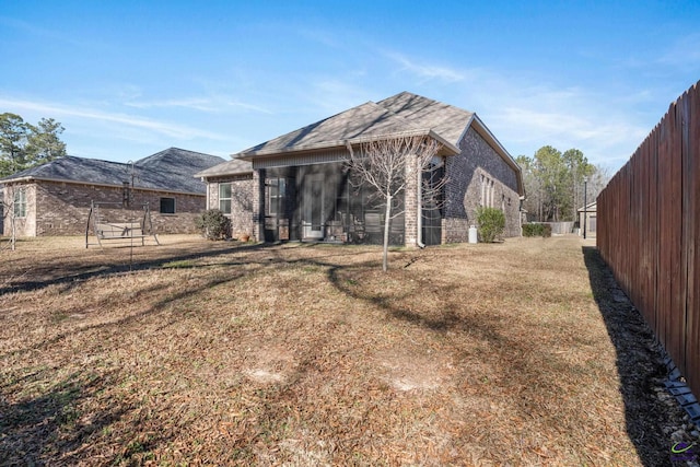 back of property featuring fence, a lawn, and brick siding