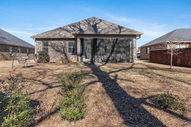 back of property with roof with shingles, a yard, brick siding, and a sunroom