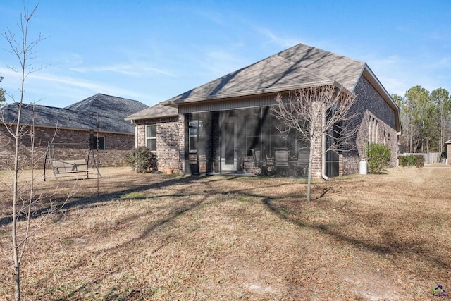 rear view of house with a lawn, brick siding, and roof with shingles