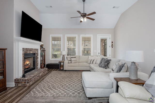 living room with a brick fireplace, lofted ceiling, a ceiling fan, visible vents, and wood finished floors