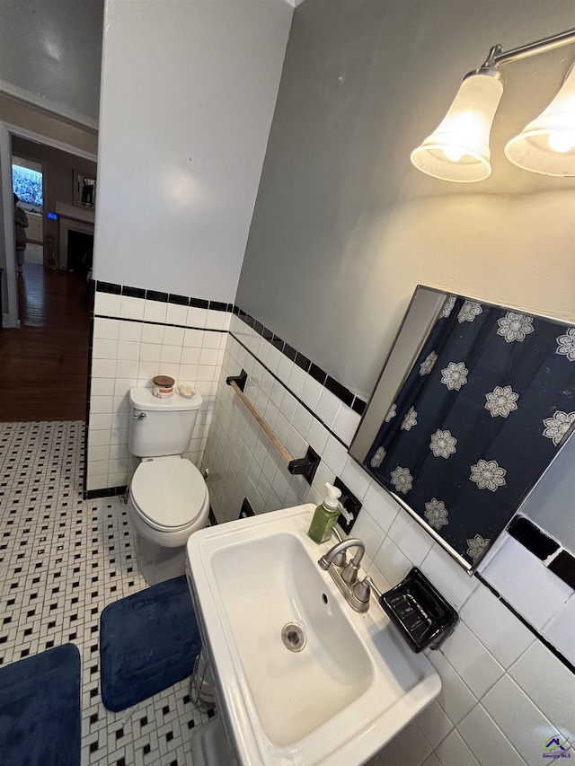 bathroom with a sink, tile walls, a wainscoted wall, and toilet