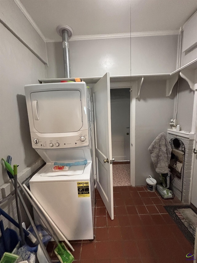 clothes washing area with laundry area, ornamental molding, dark tile patterned floors, and stacked washing maching and dryer