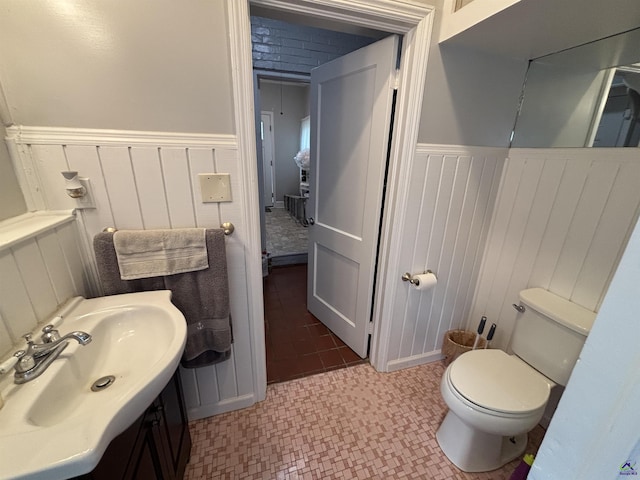 half bath featuring a decorative wall, toilet, wainscoting, and vanity