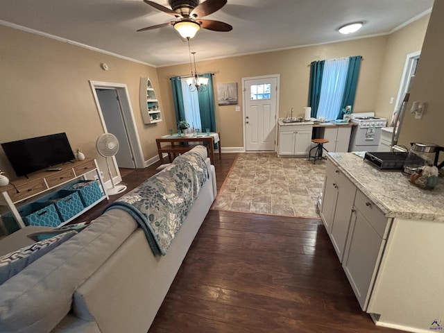 living area featuring baseboards, ornamental molding, ceiling fan with notable chandelier, and hardwood / wood-style floors