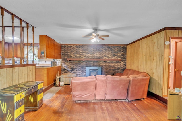 living room with crown molding, wood walls, a brick fireplace, wood finished floors, and a ceiling fan