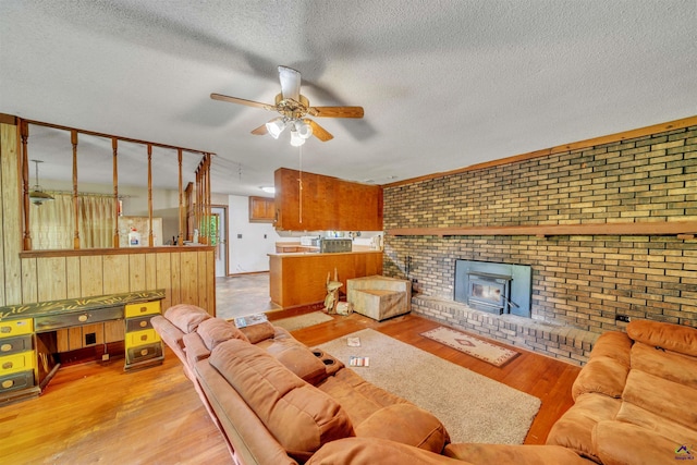 living area featuring wooden walls, ceiling fan, a textured ceiling, brick wall, and wood finished floors