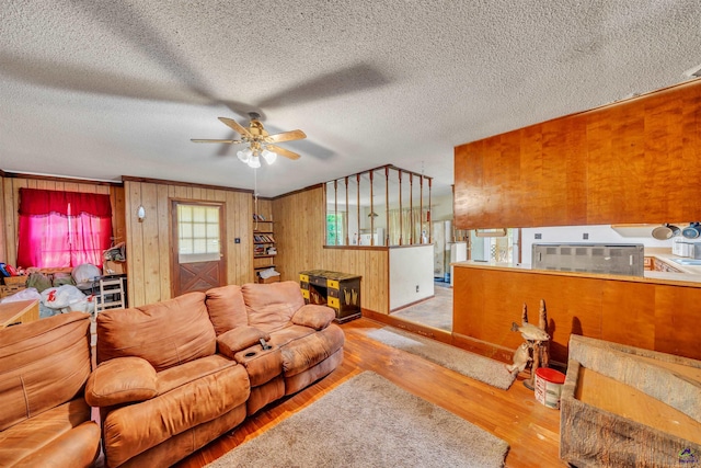 living room with wooden walls, a textured ceiling, a ceiling fan, baseboards, and wood finished floors