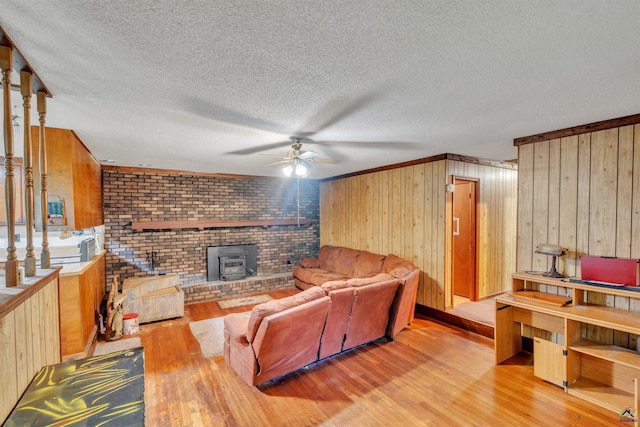 living area featuring ceiling fan, wood walls, a wood stove, and hardwood / wood-style floors