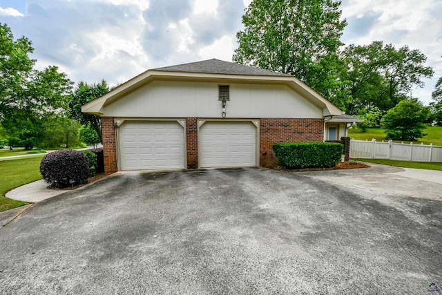 view of home's exterior featuring a garage, aphalt driveway, fence, brick siding, and a yard