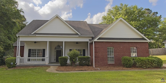 view of front of home featuring roof with shingles, brick siding, a porch, a front yard, and a ceiling fan