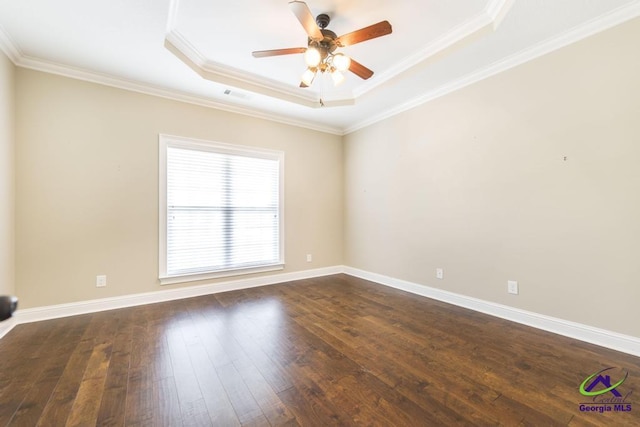 spare room with visible vents, ornamental molding, dark wood-style floors, a tray ceiling, and a ceiling fan