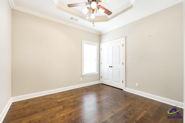 empty room with visible vents, ornamental molding, a raised ceiling, a ceiling fan, and dark wood finished floors
