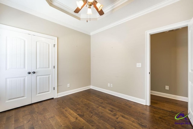 unfurnished bedroom featuring crown molding, a raised ceiling, baseboards, wood finished floors, and a closet