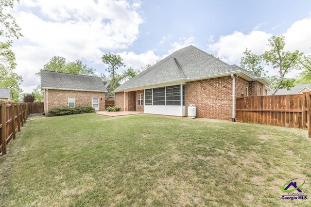 back of property featuring roof with shingles, brick siding, a fenced backyard, a patio area, and a yard