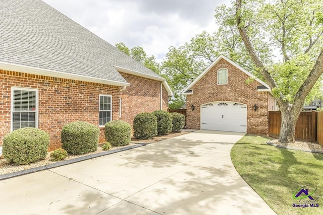 exterior space featuring fence, roof with shingles, brick siding, concrete driveway, and an attached garage