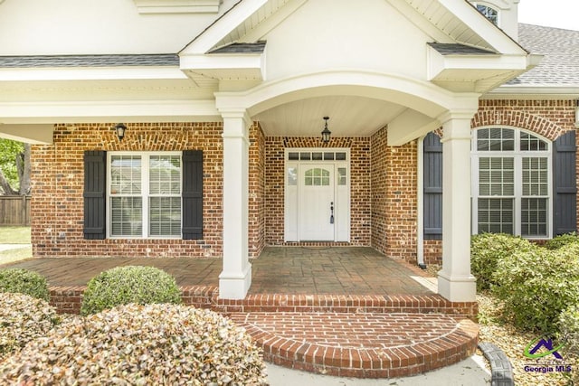 entrance to property with brick siding, roof with shingles, and covered porch