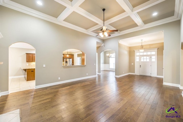 unfurnished living room featuring arched walkways, coffered ceiling, ceiling fan with notable chandelier, and hardwood / wood-style flooring