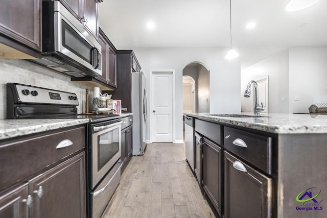 kitchen featuring dark brown cabinets, arched walkways, a sink, light wood-style flooring, and appliances with stainless steel finishes