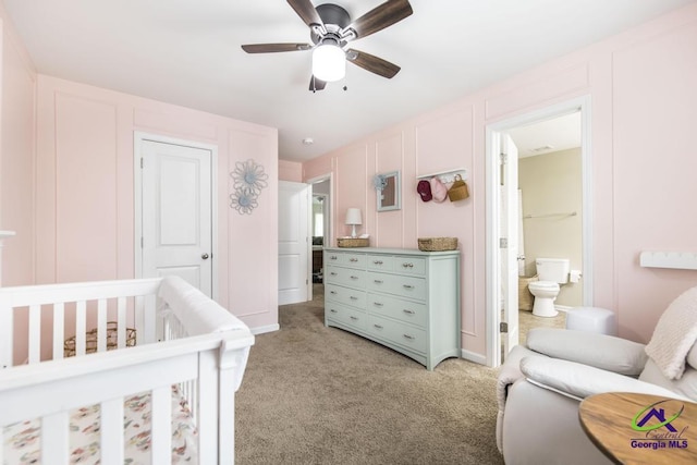 bedroom with light carpet, a crib, ensuite bath, a decorative wall, and a ceiling fan