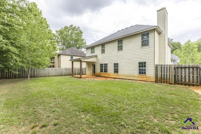 rear view of property featuring a yard, a chimney, a fenced backyard, and a patio area