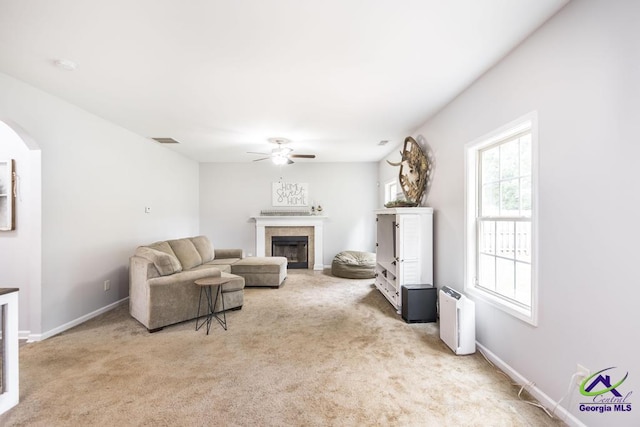 carpeted living area featuring arched walkways, a ceiling fan, baseboards, a tile fireplace, and visible vents