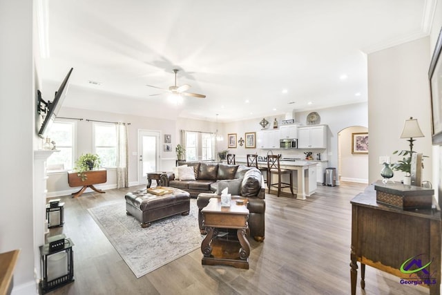 living area with baseboards, arched walkways, light wood-style flooring, and ceiling fan