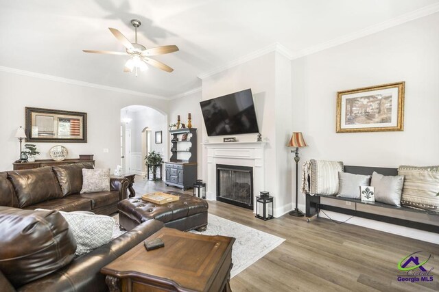 living room with a ceiling fan, crown molding, arched walkways, a fireplace, and wood finished floors