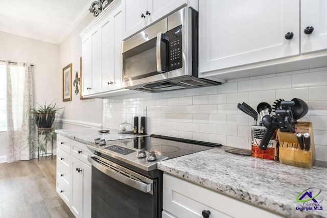 kitchen featuring light stone countertops, light wood-style floors, stainless steel appliances, white cabinetry, and ornamental molding