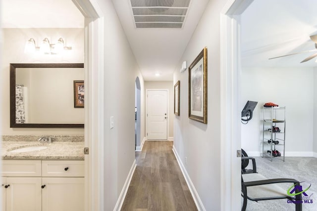 corridor featuring visible vents, arched walkways, wood finished floors, a sink, and baseboards